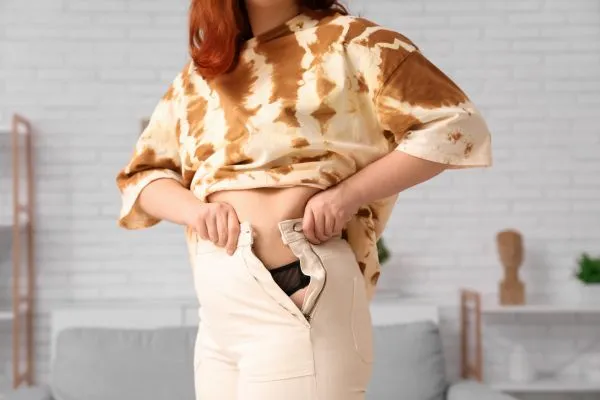 Image of woman trying to do her trousers up after pregnancy weight gain Maldon